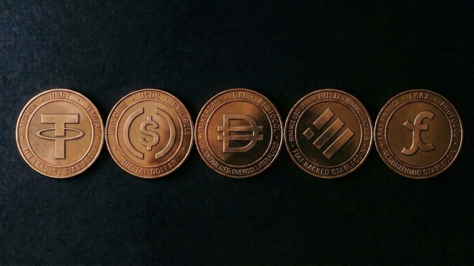 Five bronze cryptocurrency coins arranged in a row on a dark background, featuring Tether, USDC, DAI, Binance USD, and Frax USD symbols
