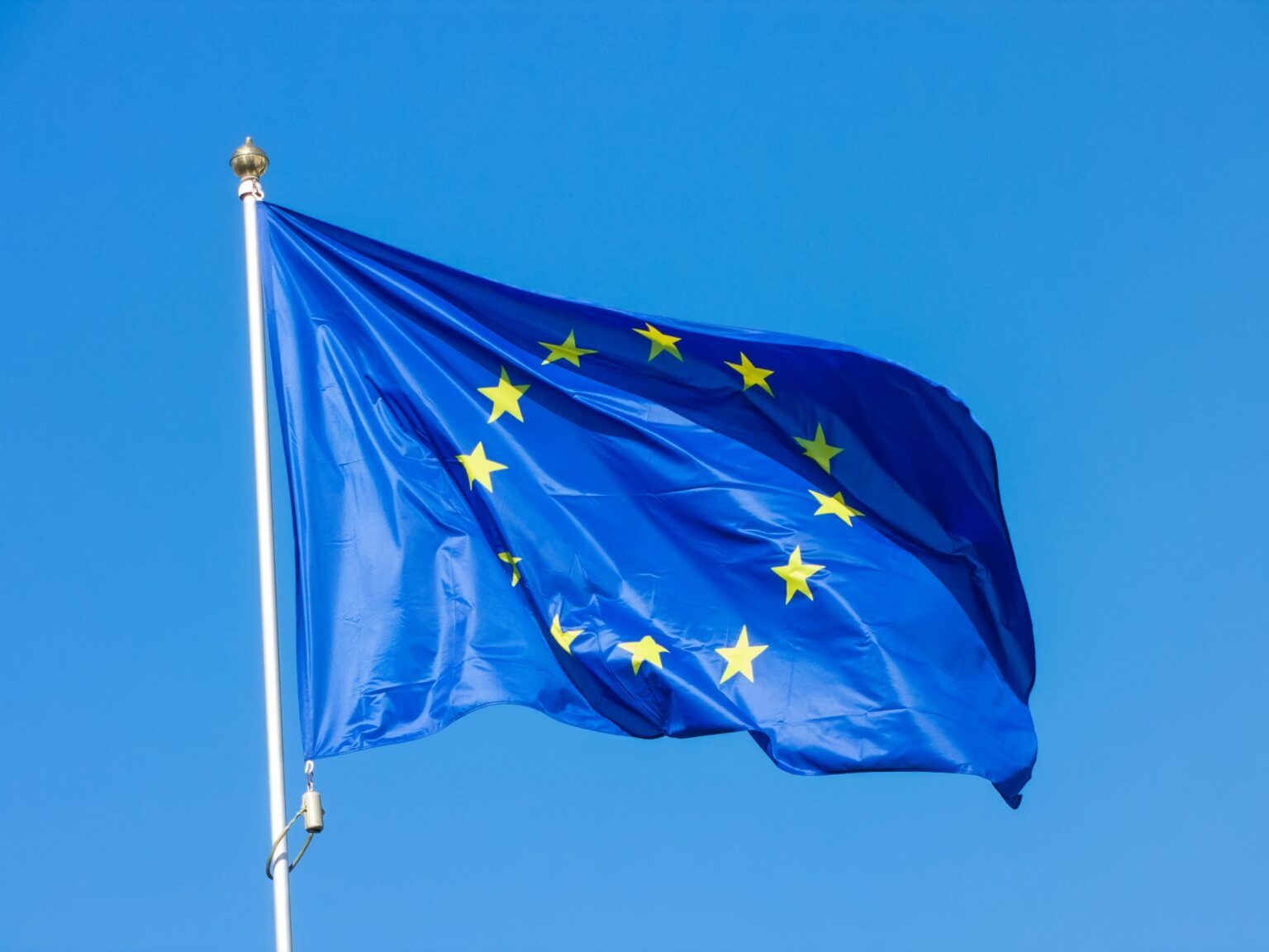 Euro Stablecoin Market Surges to $835 Million as Ethereum, Solana and Base Take 92% European Union flag, blue with a circle of yellow stars, waves on a flagpole against a clear sky