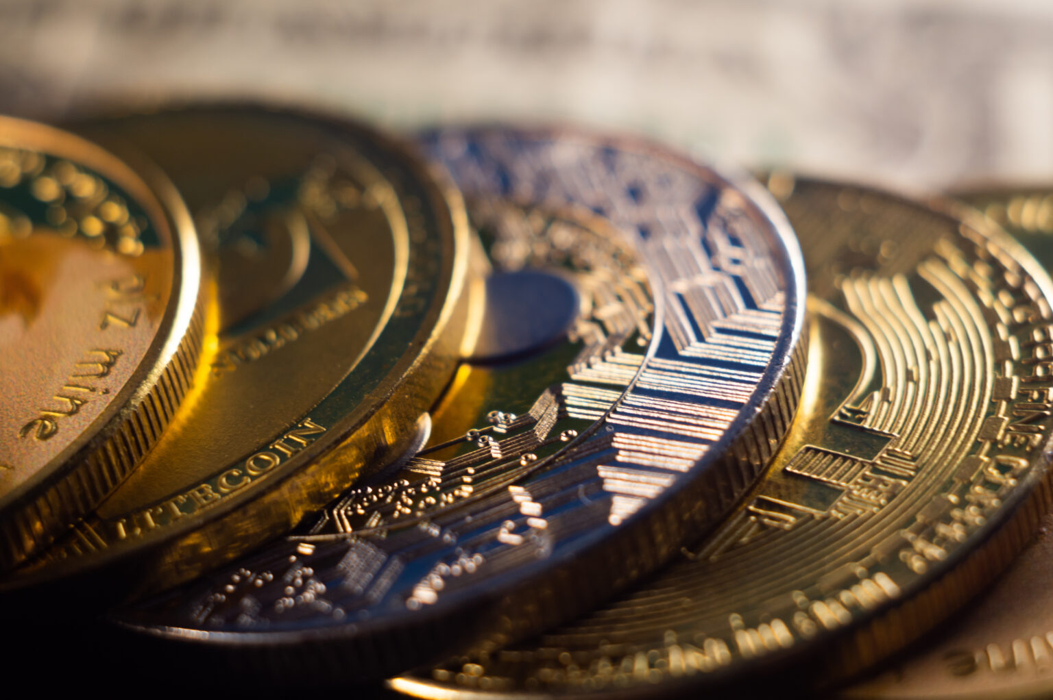 Close-up of overlapping gold and silver cryptocurrency coins, including Bitcoin, with detailed circuitry and warm lighting
